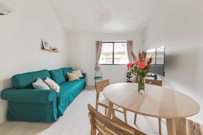 A modern living room with a teal sofa, wooden dining table, and a large window with curtains. - Located 650 meters from Tokyo Skytree, with direct access from Narita and Haneda Airports. A two-story single-family home that accommodates up to 7 guests. A 4-minute walk from the nearest station. (墨田区)