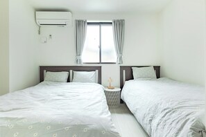 A hotel room with two beds, a window with curtains, an air conditioning unit, and a small table with a lamp. - Located 650 meters from Tokyo Skytree, with direct access from Narita and Haneda Airports. A two-story single-family home that accommodates up to 7 guests. A 4-minute walk from the nearest station. (墨田区)