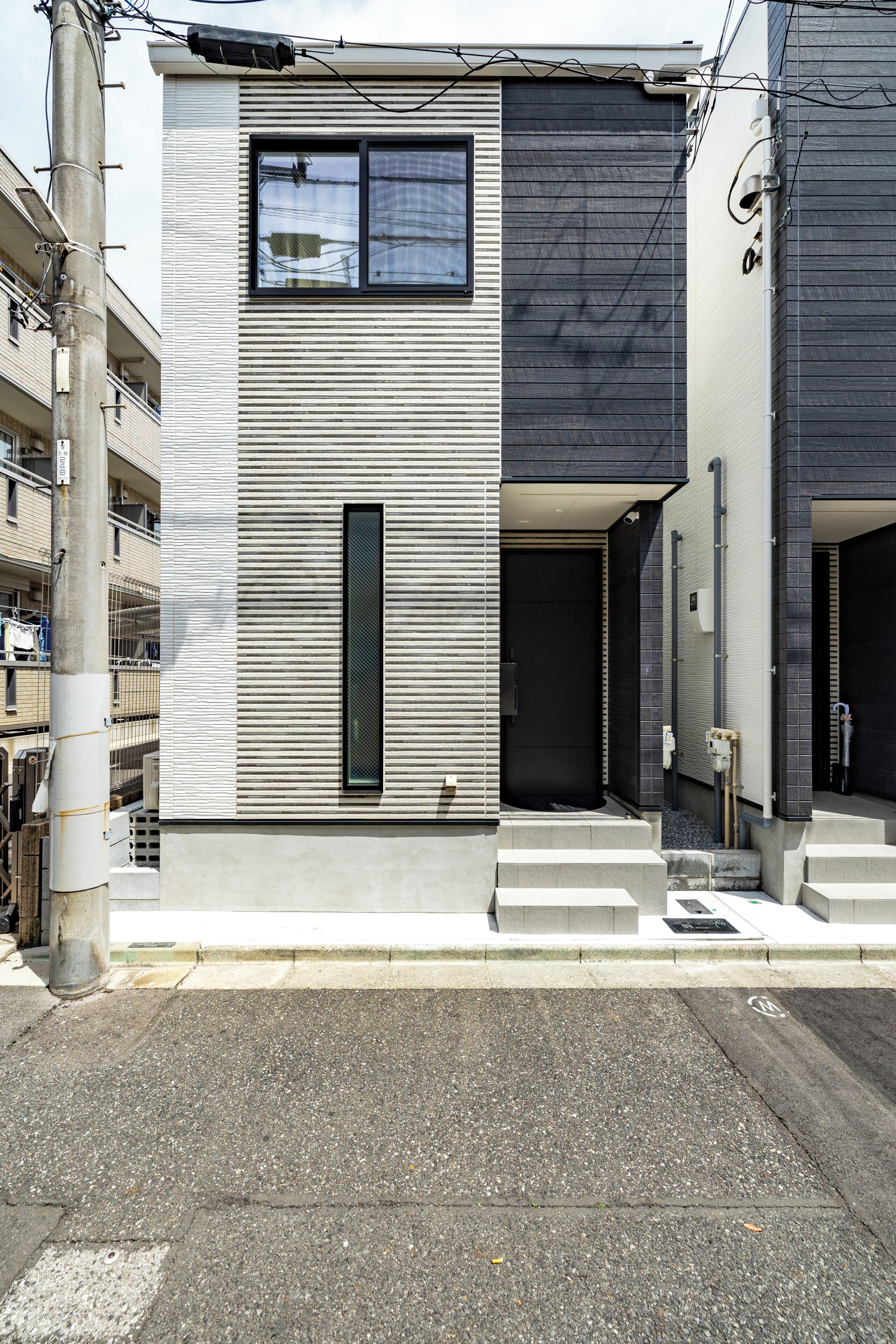 A modern two-story building with a minimalist facade, a prominent vertical window, and a clean entrance with steps.