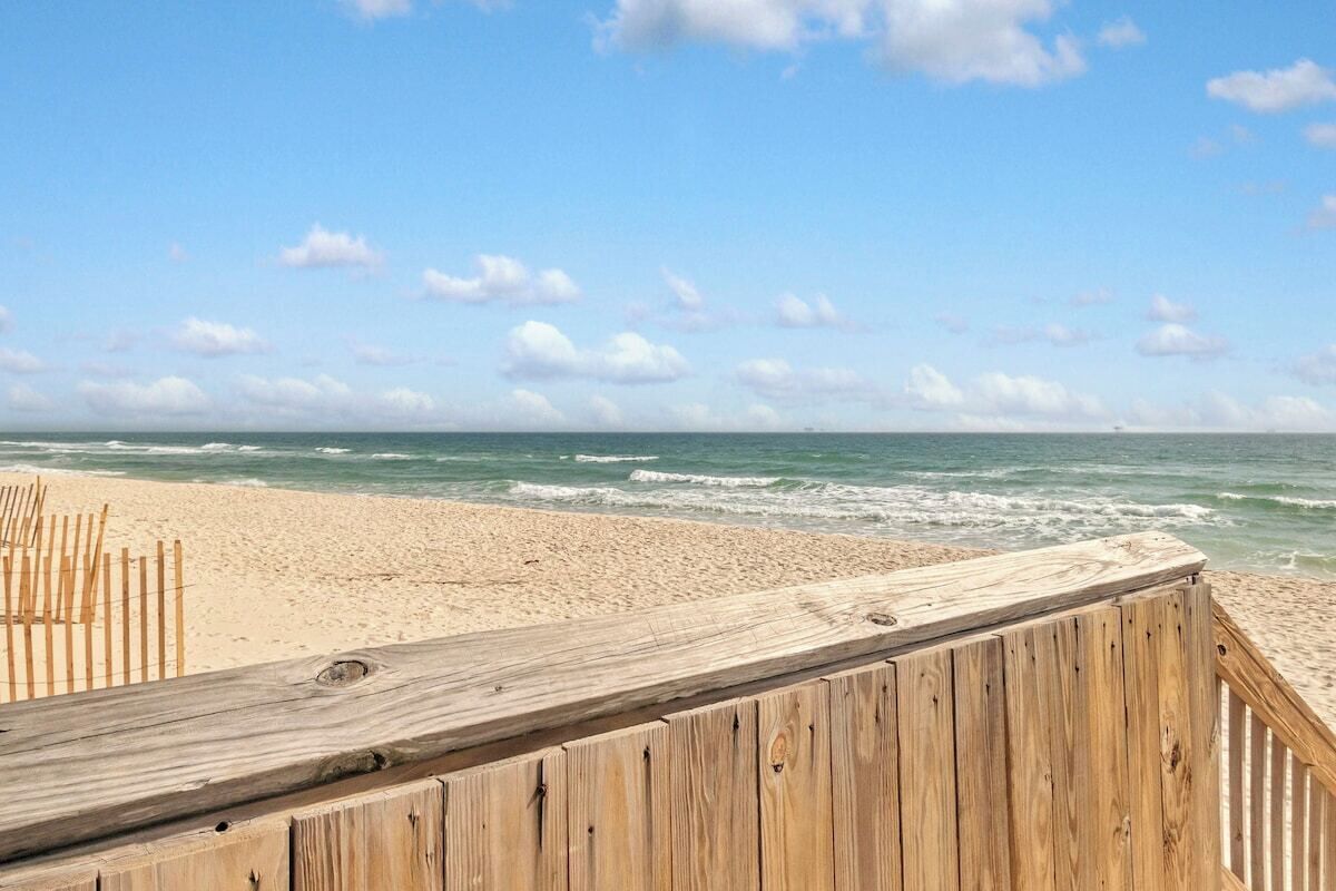 En träpromenad som leder till en sandstrand med havet i bakgrunden.