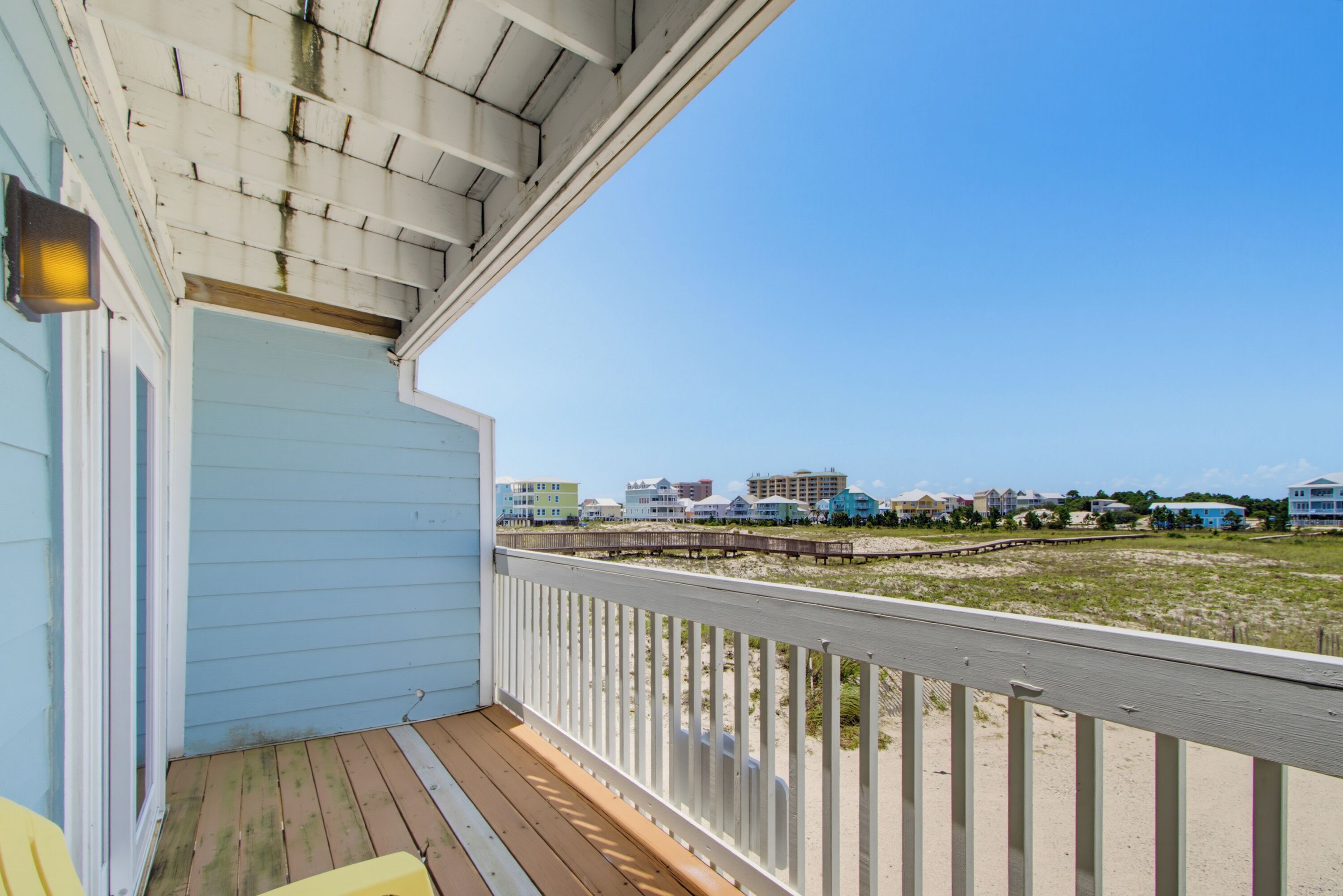 A wooden deck with a railing, a light fixture, and a view of beach houses in the distance.