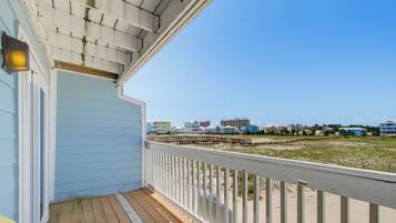 A wooden deck with a railing, a light fixture, and a view of beach houses in the distance.
