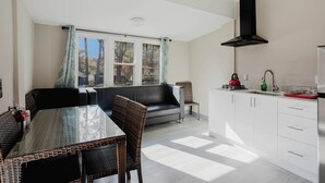 Una cocina moderna con armarios blancos, una campana extractora negra y un comedor con mobiliario de mimbre.