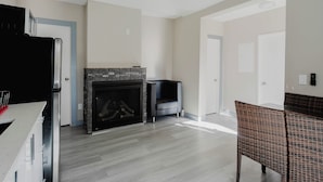Una sala de estar moderna con chimenea, un comedor con muebles de mimbre y una cocina con refrigerador negro.