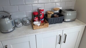 Een aanrecht met een waterkoker, een broodrooster, een mand met snacks, een suikerpot, een blikje Pringles en een koffiezetapparaat.