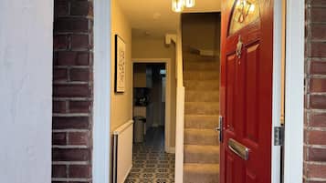 A hallway with a red door, a staircase, patterned floor tiles, a radiator, and a ceiling light fixture.
