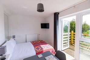 Ein Hotelzimmer mit Bett, Schreibtisch, Stuhl, Fernseher und einem Balkon mit Blick auf Grünflächen.