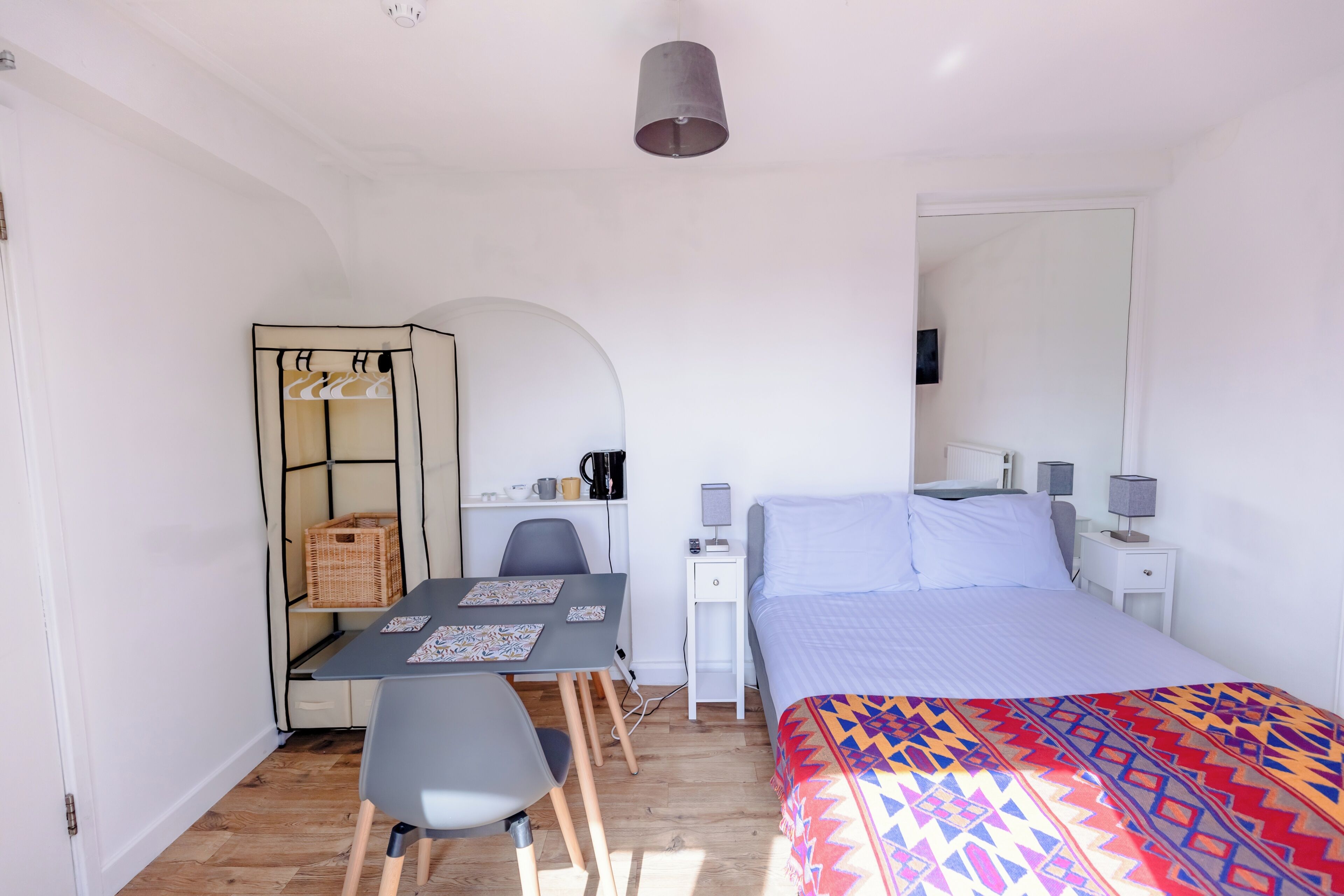 Une petite pièce bien éclairée, comprenant un lit, un bureau avec une chaise, une armoire et un miroir.