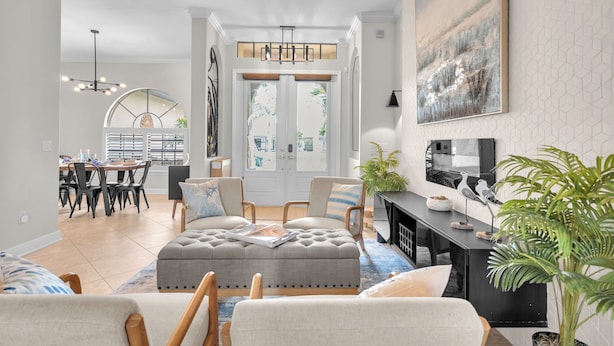 A modern living room with a grey sofa, a dining area with a table and chairs, a fireplace, and a large window with a view. - Pool Waterfall | 4BR | S. Exposure | Dogs OK (Cape Coral)