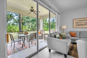 A modern living room with a sofa, chairs, a dining table, and a balcony with glass doors. - Golf & Beach Shuttle | Estero | 30 Days (Estero)