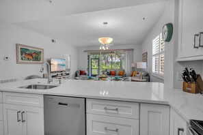 A modern kitchen with a large island, white cabinetry, and a dining area with a sofa and table. - Golf & Beach Shuttle | Estero | 30 Days (Estero)