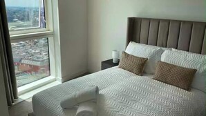 Ein Hotelzimmer mit einem großen Fenster, einem Bett mit gemusterten Laken, einem Kopfteil und einem Nachttisch mit einer Lampe.