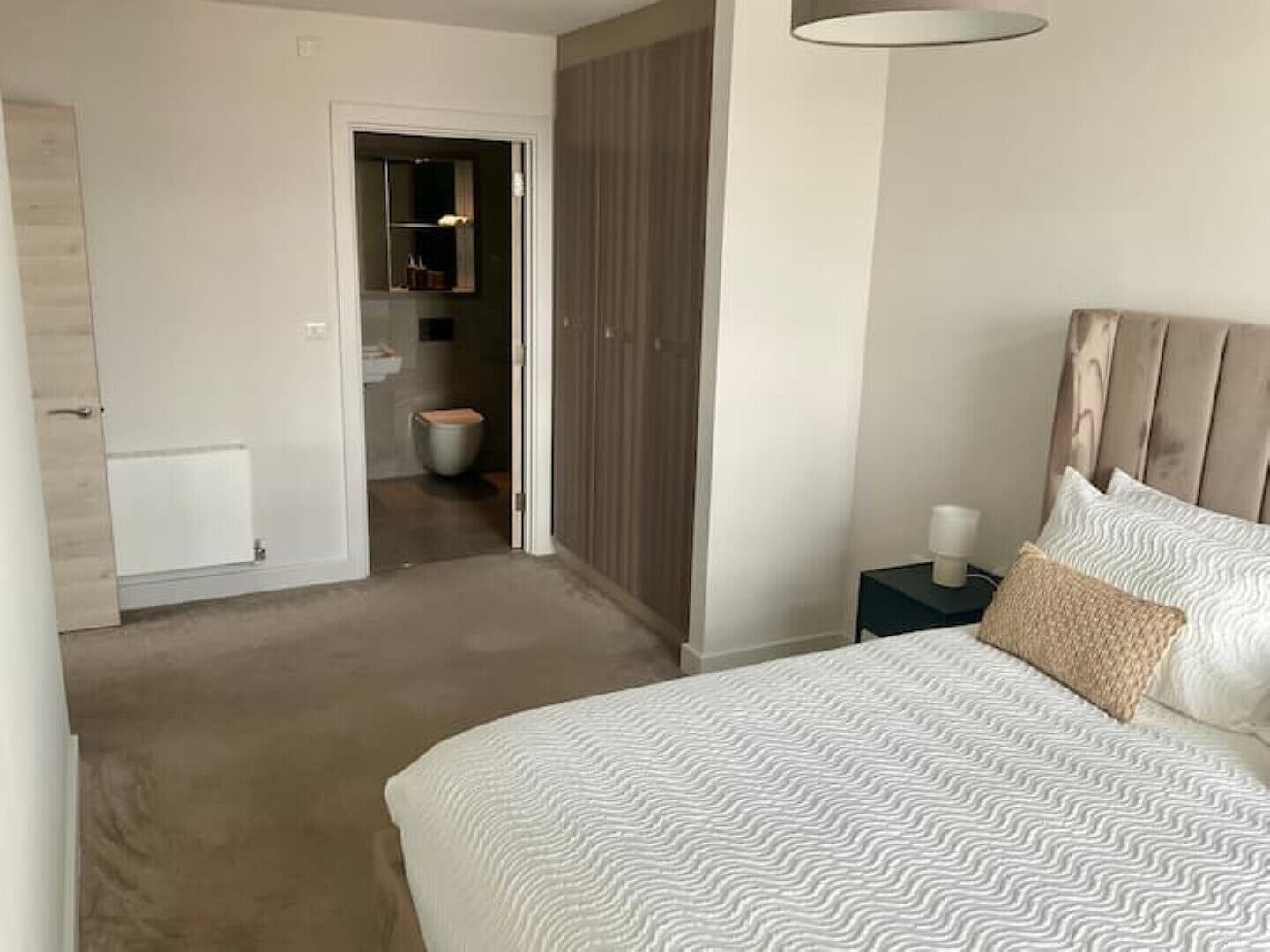 Une chambre à coucher comprenant un lit, une table de chevet et une porte donnant sur une salle de bain.