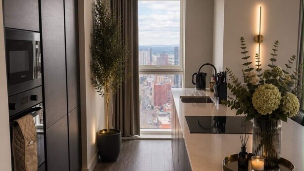 Eine moderne Küche mit Kochinsel, einem Blumentopf und Blick auf die Stadt durch ein großes Fenster.