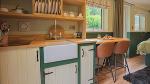 A kitchen with wooden shelves, a microwave, a sink, and two bar stools.