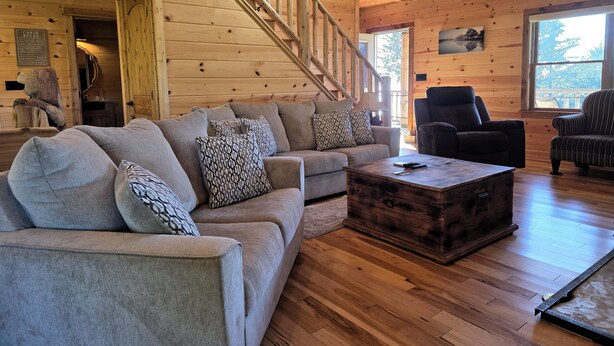 Een interieur van een chalet met een houten trap, een zithoek, een bijzettafeltje en een stoel.