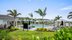 Un espace piscine avec des chaises longues, un coin salon abrité et des palmiers.