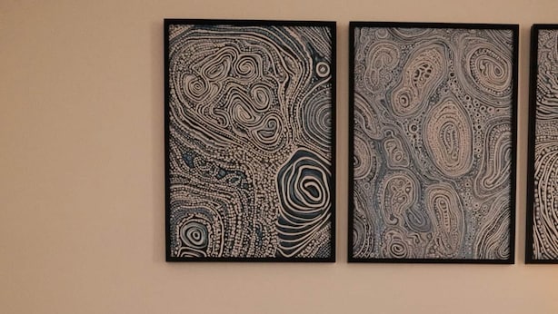 Quarto com cama, almofadas, mesa de cabeceira com um vaso e decoração na parede.
