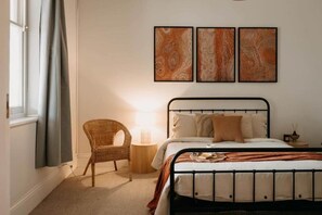 Een slaapkamer met een bed, een stoel, een nachtkastje en wanddecoratie.