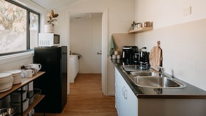 Cozinha com geladeira, micro-ondas, pia e prateleiras de madeira.