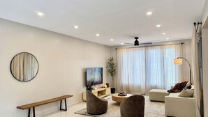 A modern living room with a bench, two armchairs, a sofa, a TV, a floor lamp, and a large window with curtains. - Private 3 Bedroom Tropical Luxury Villa · St. Kitts (Basseterre)
