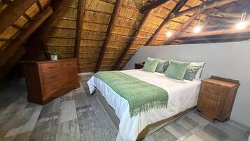 A bedroom with a sloped ceiling, a bed with a green blanket, a wooden dresser, and a nightstand.