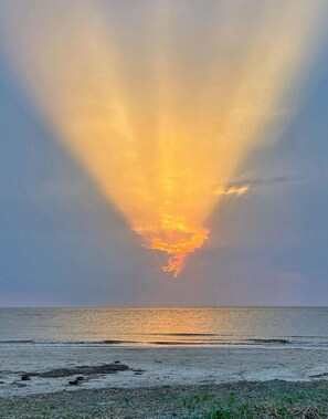Ein Sonnenuntergang über einem Strand mit ruhigem Wasser und wolkenlosem Himmel.