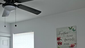 A bedroom with a bed, a ceiling fan, a window with blinds, a bedside table with a vase, and a wall with a motivational quote. - Lovely 2-bedroom house with AC near charming Delaware Bay (Lower Township)