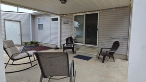 Un patio couvert aménagé avec du mobilier d’extérieur, notamment un fauteuil à bascule et une chaise, situé près d’une porte-fenêtre coulissante.