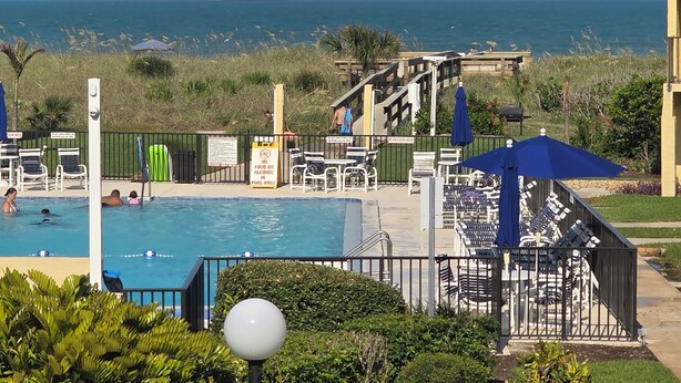 Un espace piscine avec des chaises longues, un panneau indiquant qu’il est interdit d’y apporter de la nourriture ou des boissons alcoolisées, et une vue sur l’océan.