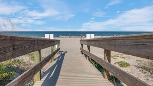 Une promenade en bois menant à une plage, avec un ciel dégagé.