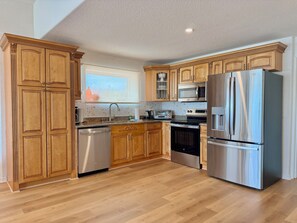 A kitchen with wooden cabinets, stainless steel appliances, and a window. - Direct Oceanfront House – Newly Renovated with Stunning Views-Sleeps 5-2bed2bath (Flagler Beach)