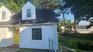 A small white house with a yellow door, a small porch, and a fenced yard.