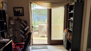 A room with a tiled floor, a black office chair, a bookshelf, a door leading outside, and a small rug.