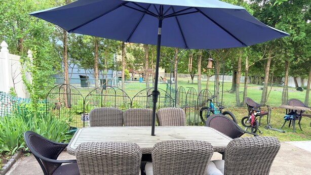 A patio with a table and chairs, surrounded by greenery and a fence.