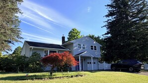 A two-story house with a front yard, a driveway, and a black SUV parked in the driveway.