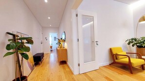 Um corredor com piso de madeira, uma porta branca, uma cadeira amarela e uma planta.