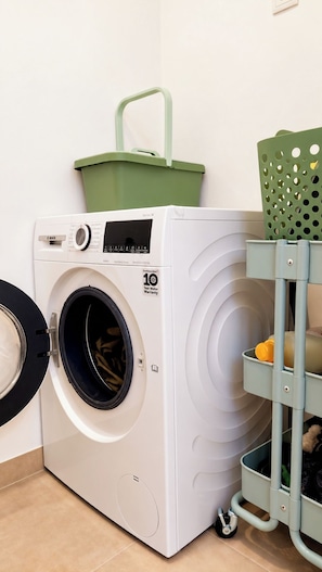 A front-loading washing machine with a 10-year motor warranty, a green basket on top, and a green laundry basket on the right. - Spacious apartment in Lisbon | 2 bedrooms with AC (Lisbon)