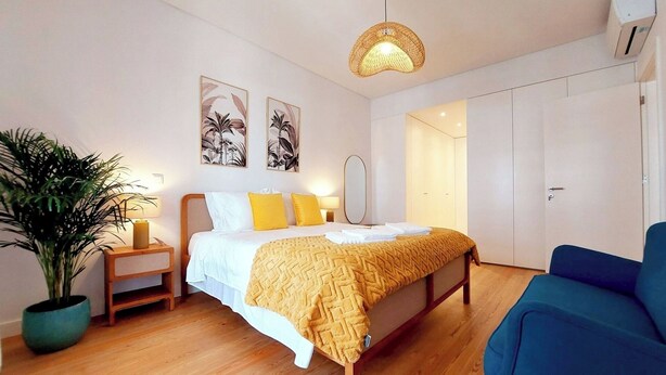 Quarto com cama, mesas de cabeceira, planta em vaso, luminária pendente e guarda-roupa.