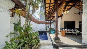 Un'area piscina con idromassaggio, posti a sedere e piante tropicali.
