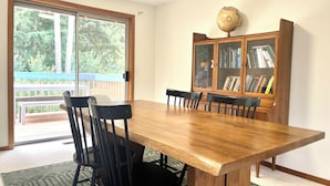 Zona pranzo con tavolo e sedie in legno, una libreria e vista su una terrazza esterna tramite una porta scorrevole in vetro.