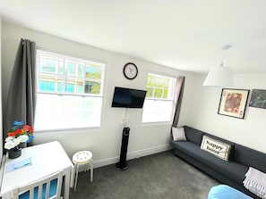 A room with a sofa, a small table, a TV, a clock, and a window with curtains. - Crown House Kings Cross Flat 2 / Sleeps up to 8 (London)