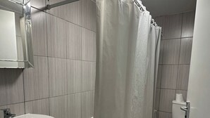 A bathroom with a shower curtain, sink, toilet, and a mirror. - House Sleeps 22 with Wifi (London)
