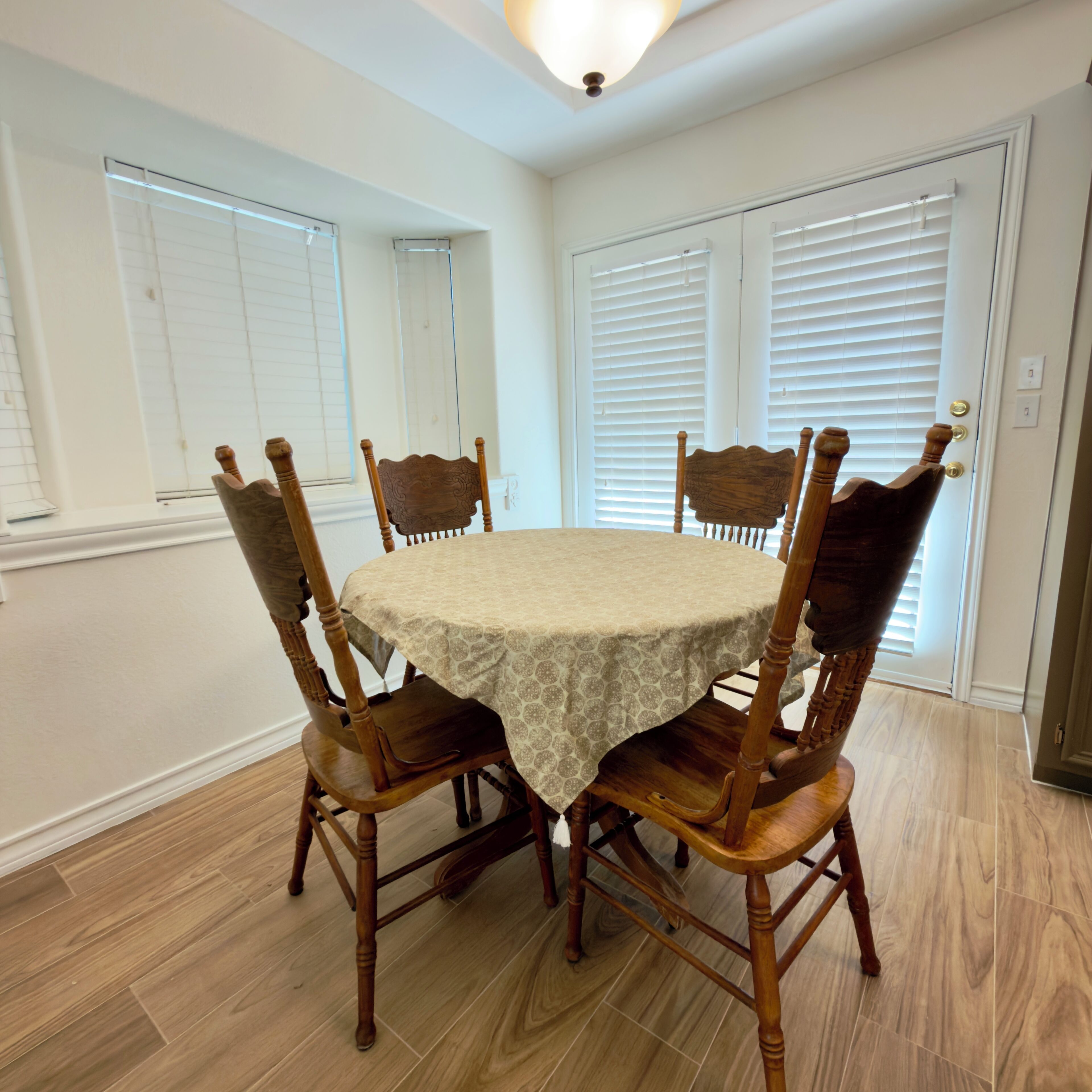 A dining area with a round table, four wooden chairs, and a light-colored tablecloth.