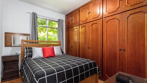 A bedroom with a bed, wooden wardrobe, window, and a nightstand. - RJ JACAREPAGUÁ - Cozy and spacious apartment. We accept small pets. (Rio de Janeiro)