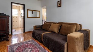 A living room with a sofa, a wooden cabinet, a patterned rug, and a mirror on the wall. - RJ JACAREPAGUÁ - Cozy and spacious apartment. We accept small pets. (Rio de Janeiro)