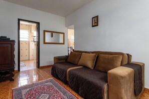 A living room with a brown sofa, a wooden cabinet, a mirror, and a patterned rug. - RJ JACAREPAGUÁ - Cozy and spacious apartment. We accept small pets. (Arraial do Cabo)