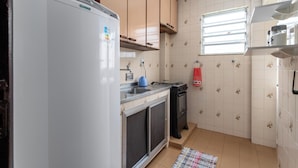 A compact kitchen with a refrigerator, stove, sink, and a window with blinds. - RJ JACAREPAGUÁ - Cozy and spacious apartment. We accept small pets. (Rio de Janeiro)