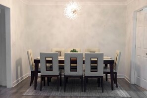 Une salle à manger avec une table ronde et six chaises, un lustre et une porte sur le côté droit.