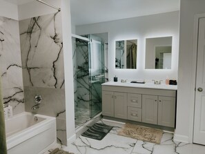 Une salle de bain avec un mur en marbre, une douche en verre, une baignoire et un meuble-lavabo avec un miroir.